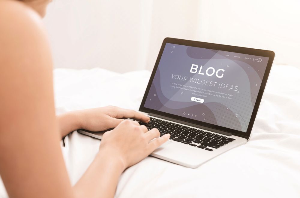 Osoba piše blog na laptopu dok sedi na krevetu