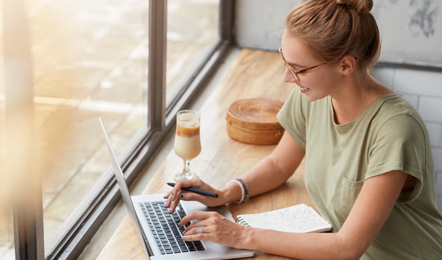 Žena radi na laptopu i zapisuje beleške dok planira kako da privuče prve čitaoce na blog